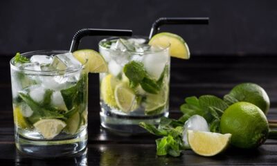 Dois copos de mojito com gelo, hortelã, limão, canudos pretos em mesa escura