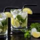 Dois copos de mojito com gelo, hortelã, limão, canudos pretos em mesa escura