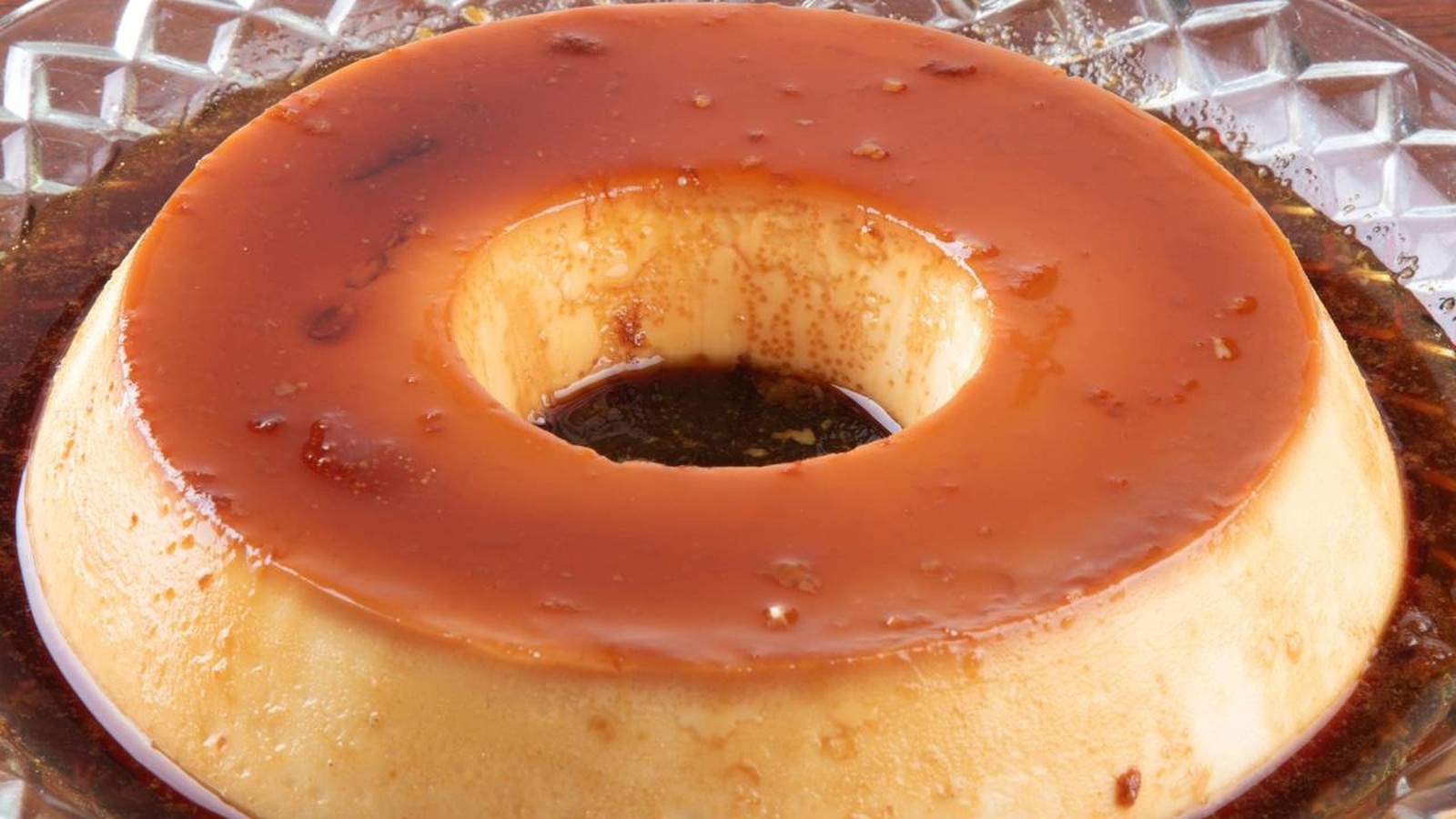 Pudim de leite condensado em forma de anel com calda de caramelo dourada em prato de vidro