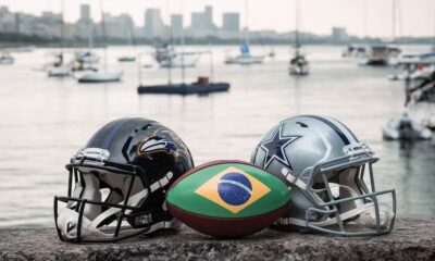 Capacete preto Ravens, capacete cinza Cowboys e bola do Brasil com baía ao fundo