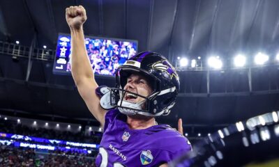 Jogador do Baltimore Ravens em uniforme roxo comemorando, capacete com 'RAVENS', patch 'RIO', em estádio