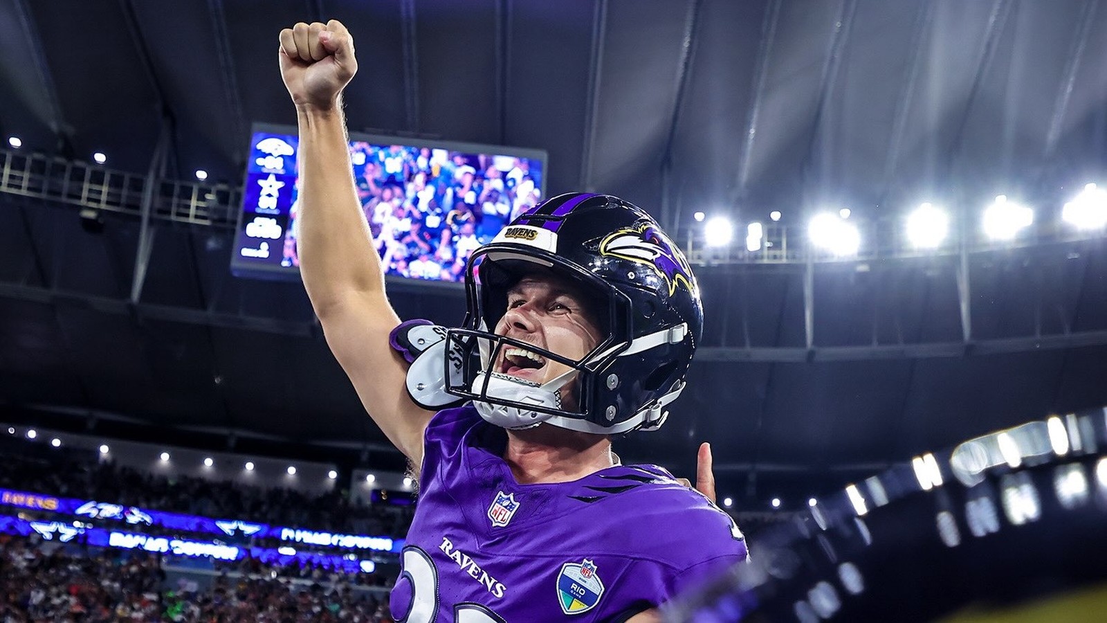 Jogador do Baltimore Ravens em uniforme roxo comemorando, capacete com 'RAVENS', patch 'RIO', em estádio
