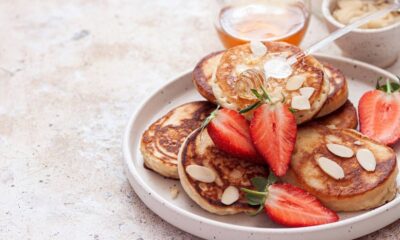 Pancakes com amêndoas, morangos e mel, servidos em prato branco com fundo desfocado