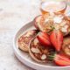 Pancakes com amêndoas, morangos e mel, servidos em prato branco com fundo desfocado