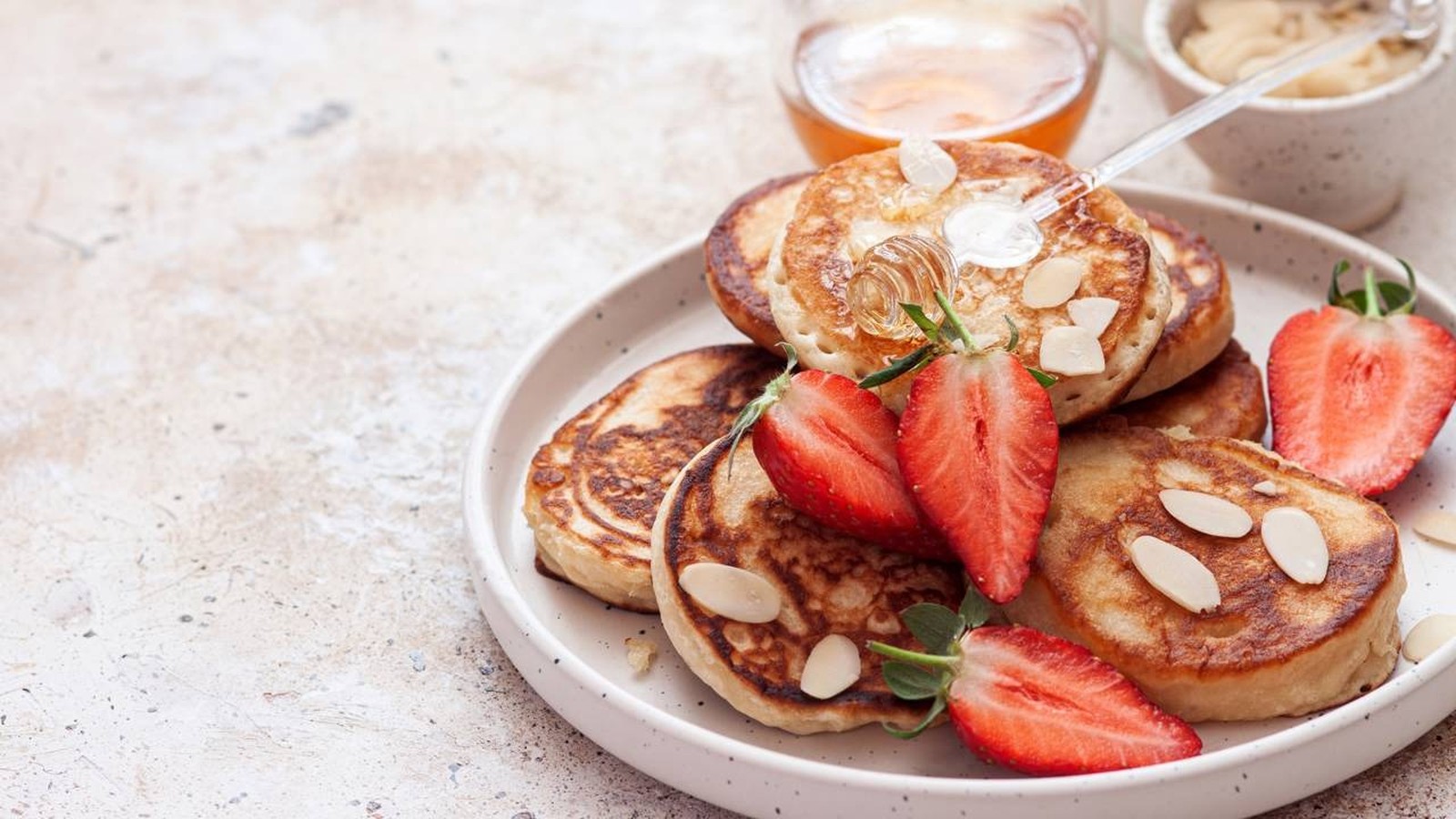 Pancakes com amêndoas, morangos e mel, servidos em prato branco com fundo desfocado