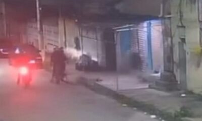 Câmera de segurança noturna mostra rua, moto vermelha, carro e duas figuras escuras