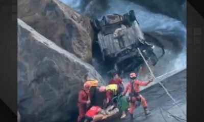 Resgatistas socorrem vítima de acidente em ribanceira com carro capotado e água agitada.