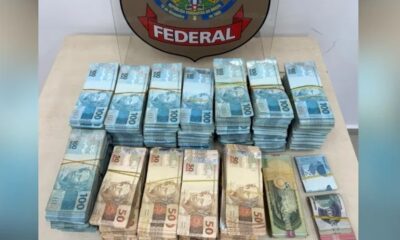 Pilhas de notas de R$100 e R$50 reais sobre mesa com escudo da Polícia Federal
