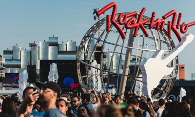 Multidão em festival, com letreiro vermelho 'Rock in Rio', guitarra branca e globo metálico