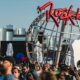 Multidão em festival, com letreiro vermelho 'Rock in Rio', guitarra branca e globo metálico