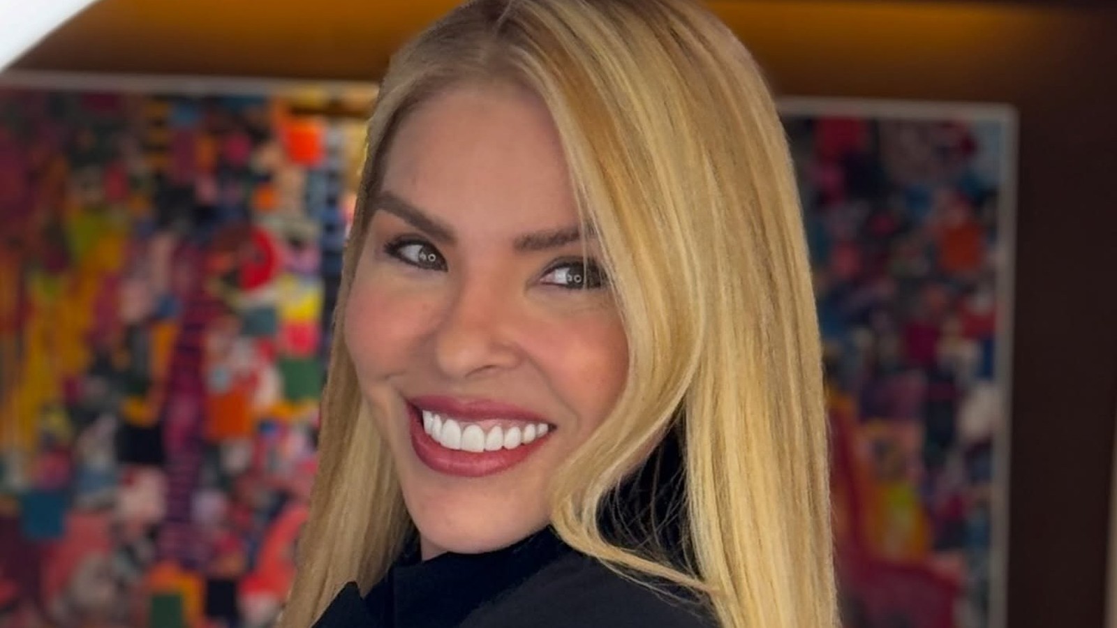 Mulher loira sorridente com cabelo longo e maquiagem leve olhando para a câmera