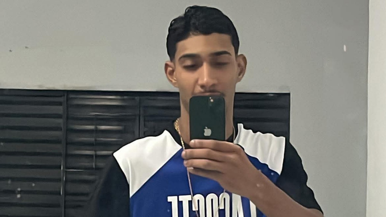 Jovem masculino tira selfie no espelho, segurando smartphone, usa corrente dourada