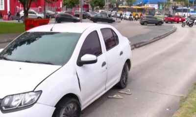 Carro sedan branco danificado com chinelos na rua, em ambiente urbano com tráfego
