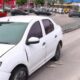 Carro sedan branco danificado com chinelos na rua, em ambiente urbano com tráfego