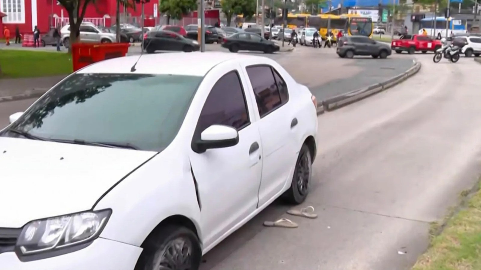 Carro sedan branco danificado com chinelos na rua, em ambiente urbano com tráfego