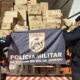 Dois policiais militares seguram bandeira PMERJ, com caixas "brf", "FLORA" em caminhão