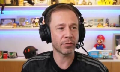 Tiago Leifert usando fones de ouvido e microfone, com fundo de prateleiras iluminadas