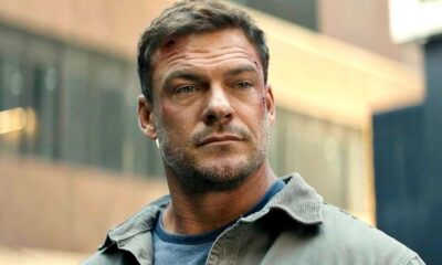Rosto do ator Alan Ritchson em close-up, com arranhões e barba, vestindo jaqueta