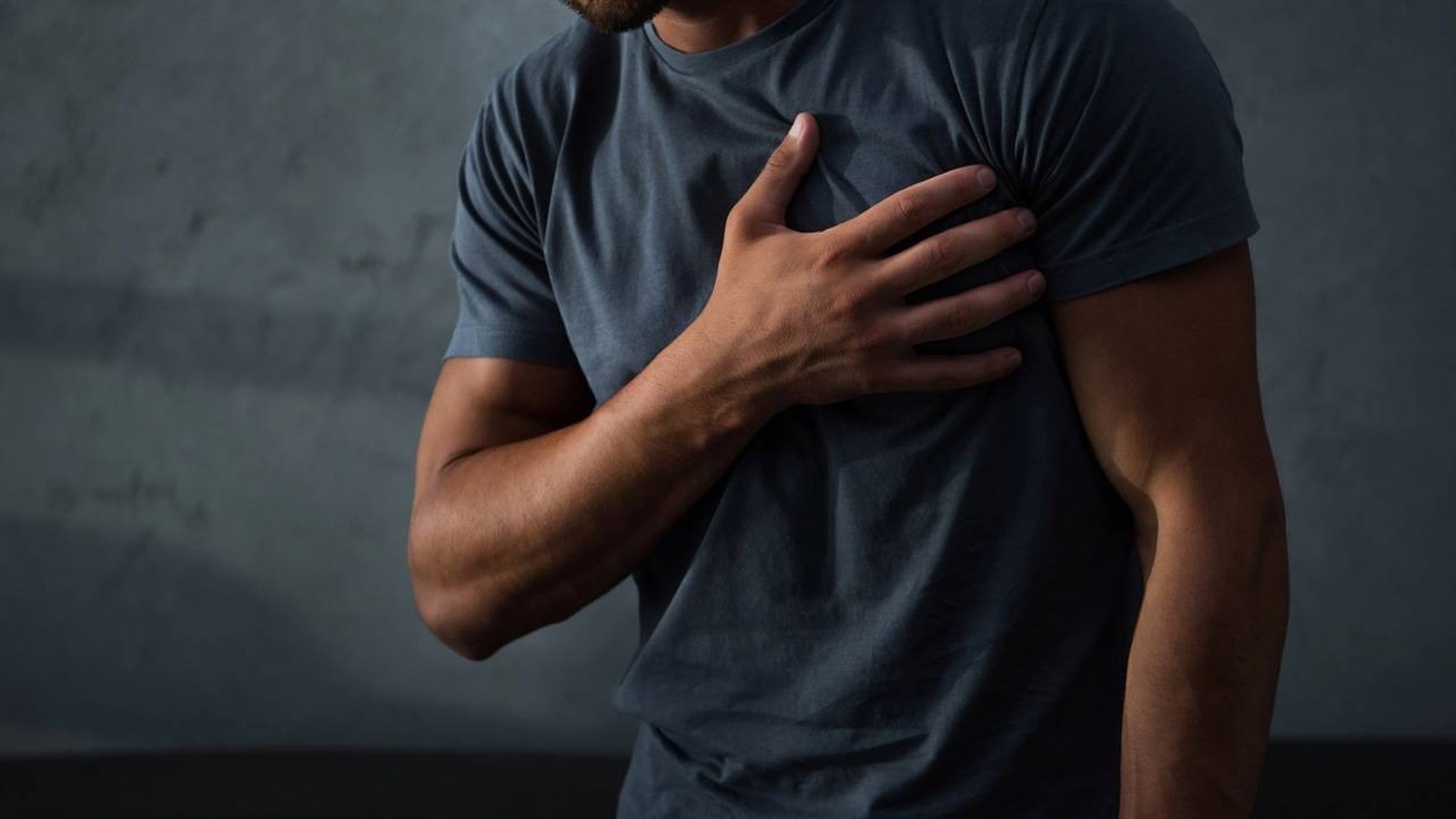 Homem de camiseta escura segura o lado esquerdo do peito com a mão direita