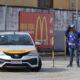Carro de autoescola prateado em pista de exames, homem em colete azul e cones amarelos