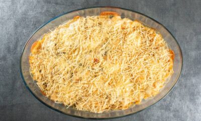 Fricassê de frango em travessa oval de vidro, coberto com queijo e batata palha dourada