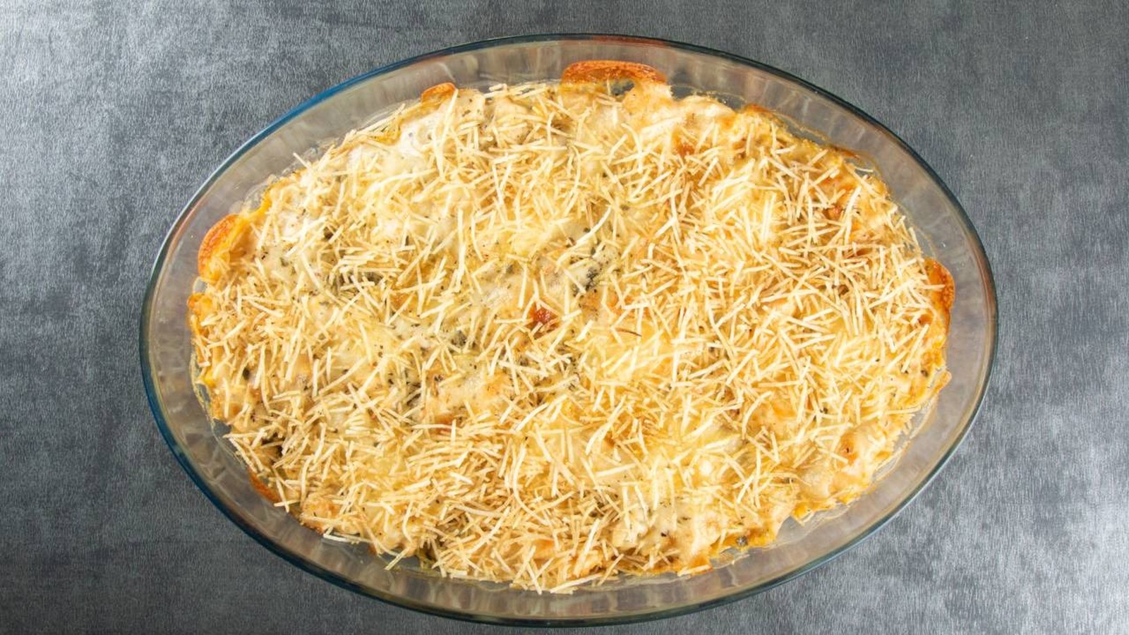 Fricassê de frango em travessa oval de vidro, coberto com queijo e batata palha dourada