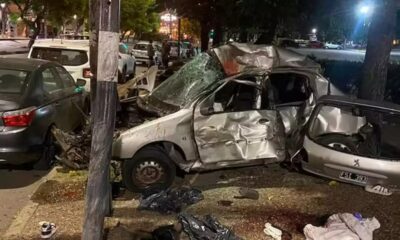 Carro prata destruído após colisão, outro veículo danificado e destroços na rua noturna