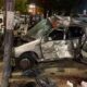 Carro prata destruído após colisão, outro veículo danificado e destroços na rua noturna