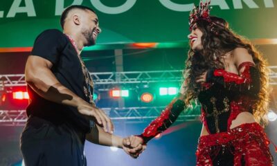 Anitta e Mestre Fafá sorrindo, de mãos dadas, em palco iluminado com luzes coloridas
