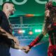 Anitta e Mestre Fafá sorrindo, de mãos dadas, em palco iluminado com luzes coloridas