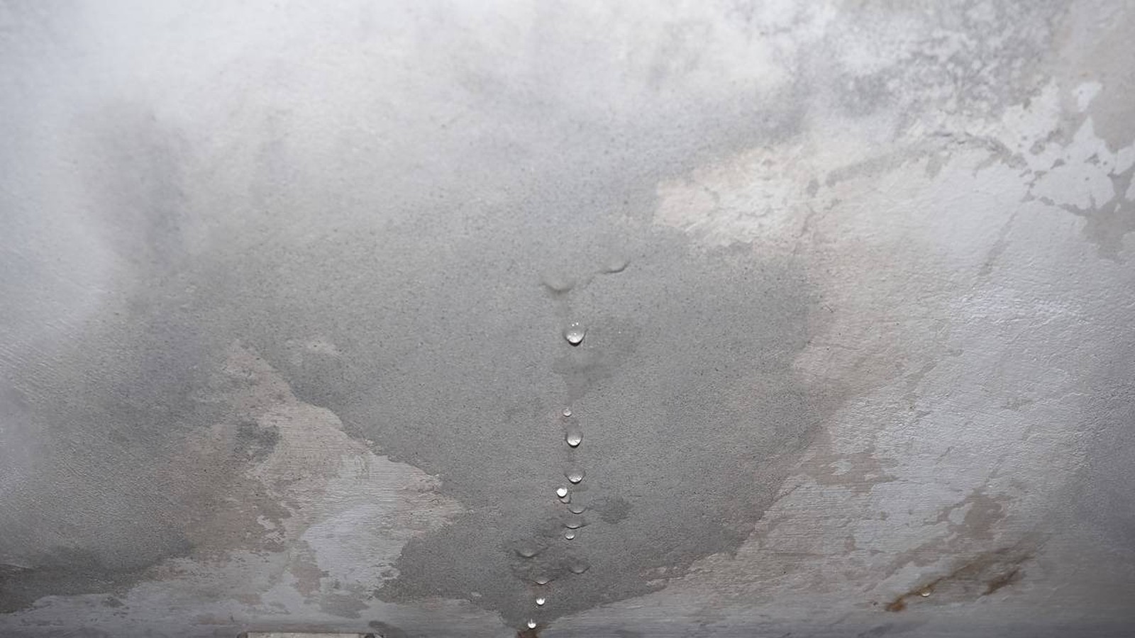 Teto de concreto com manchas de umidade e várias gotas de água pingando