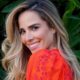 Close-up de mulher sorrindo, cabelo loiro, blusa laranja estampada, fundo de folhas verdes