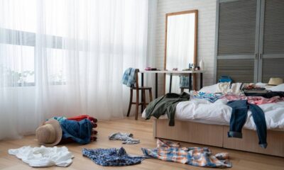 Quarto bagunçado: roupas espalhadas no chão, cama, cadeira; espelho, cortinas brancas
