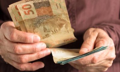 Mãos enrugadas segurando cédulas de 50 reais
