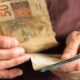 Mãos enrugadas segurando cédulas de 50 reais