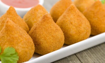 Coxinhas douradas em travessa branca, com molho vermelho e erva verde em fundo desfocado