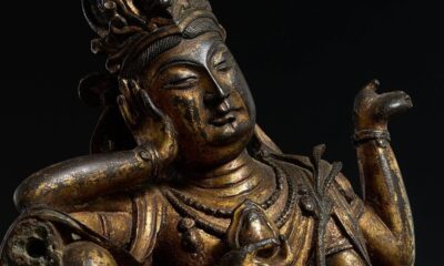 Close-up de uma antiga estátua budista de bronze dourado com rosto sereno e mão erguida