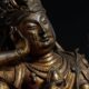 Close-up de uma antiga estátua budista de bronze dourado com rosto sereno e mão erguida