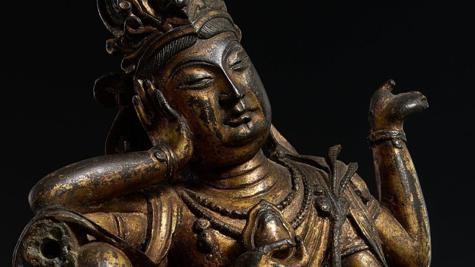 Close-up de uma antiga estátua budista de bronze dourado com rosto sereno e mão erguida