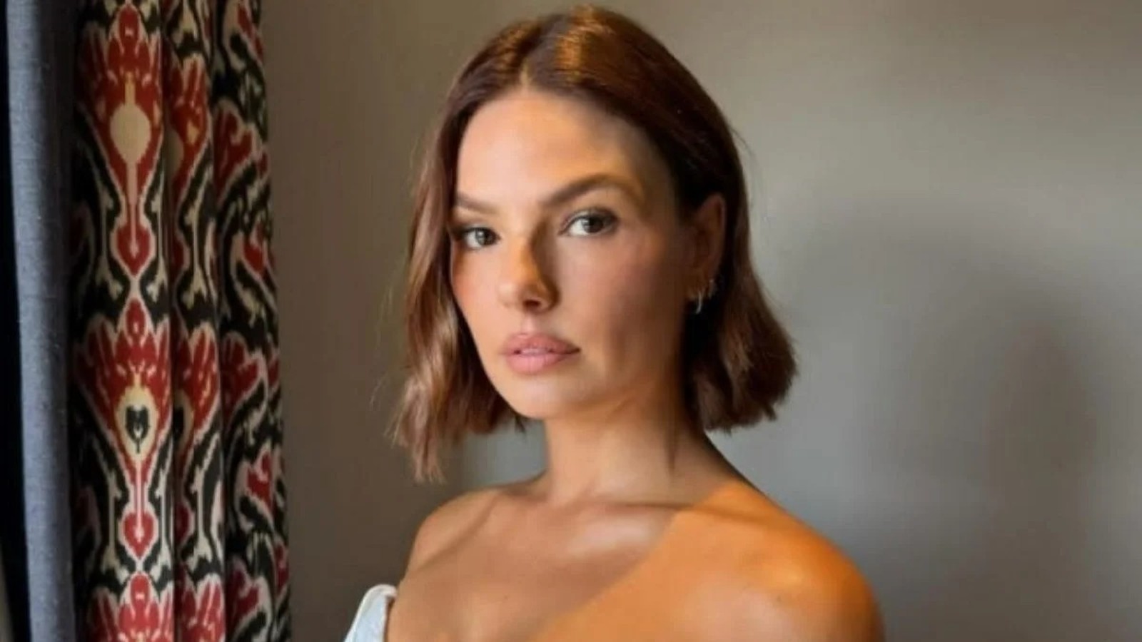 Close-up de Isis Valverde, cabelo castanho curto, olhando para a câmera com fundo de cortina estampada