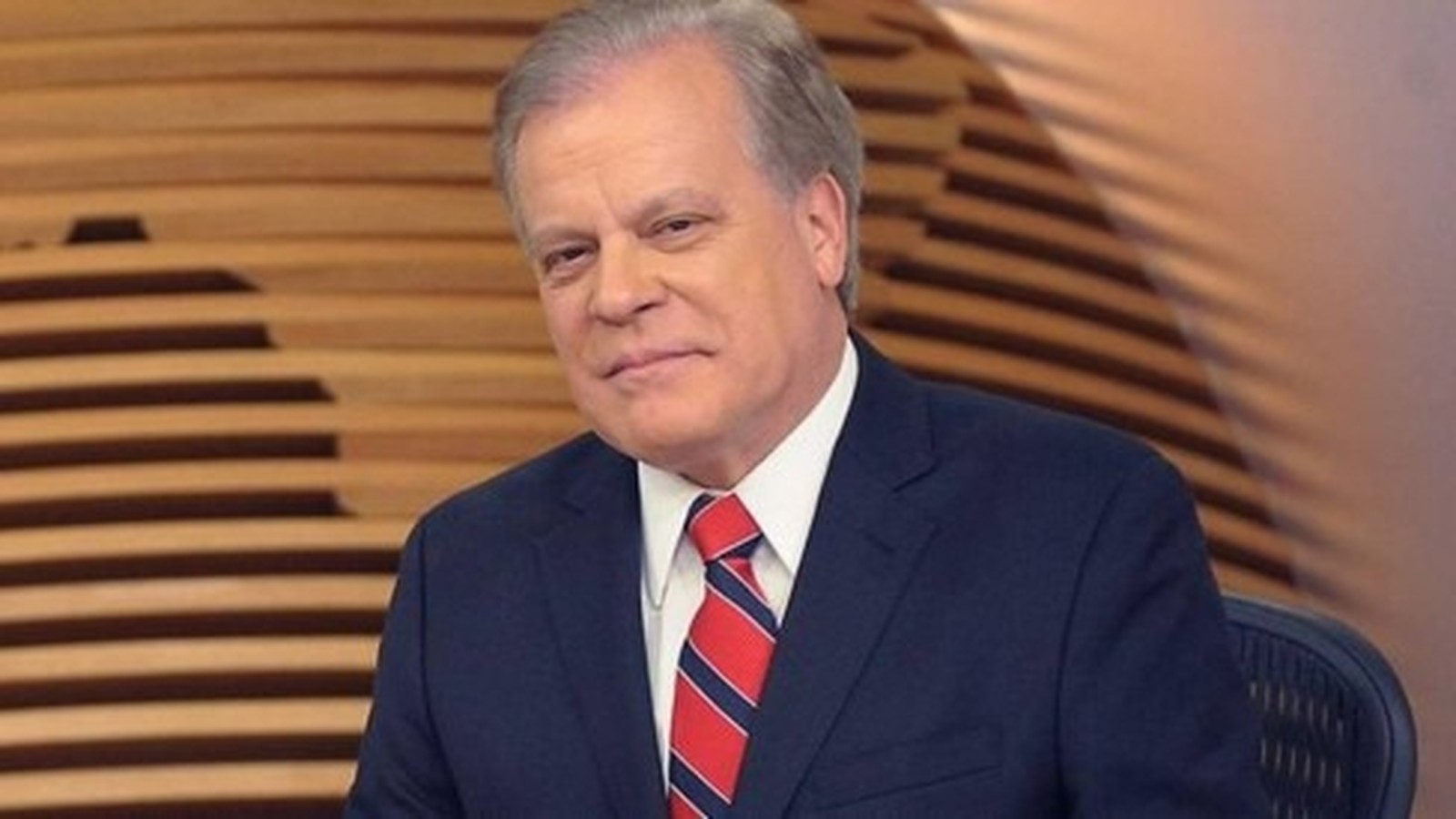 Jornalista Chico Pinheiro, cabelos grisalhos, terno azul escuro e gravata listrada, em estúdio