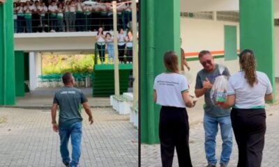 Motorista sorri emocionado recebendo presentes de alunas enquanto estudantes aplaudem em escola