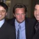 Matt LeBlanc, Matthew Perry e David Schwimmer, sorrindo, em ternos escuros, posando.