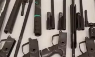 Componentes de armas de fogo de alto calibre, como fuzis, dispostas sobre uma superfície branca