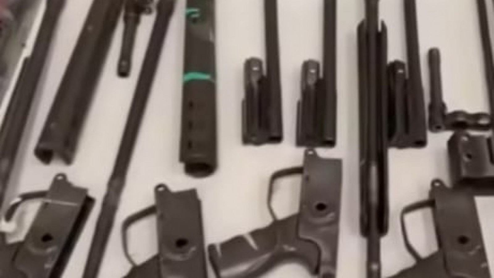 Componentes de armas de fogo de alto calibre, como fuzis, dispostas sobre uma superfície branca