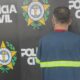 Homem de costas em camiseta azul com faixas refletivas, em frente ao logo da Polícia Civil do Rio de Janeiro