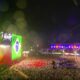 Vista aérea noturna do palco principal do Rock in Rio com telões exibindo a bandeira do Brasil e texto