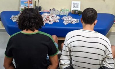 Dois homens de costas, com pilhas de pacotes, garrafas e dois rádios em mesa azul