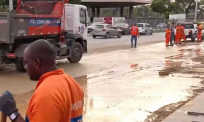Trabalhadores uniformizados e caminhão Comlurb em rua com água e lama