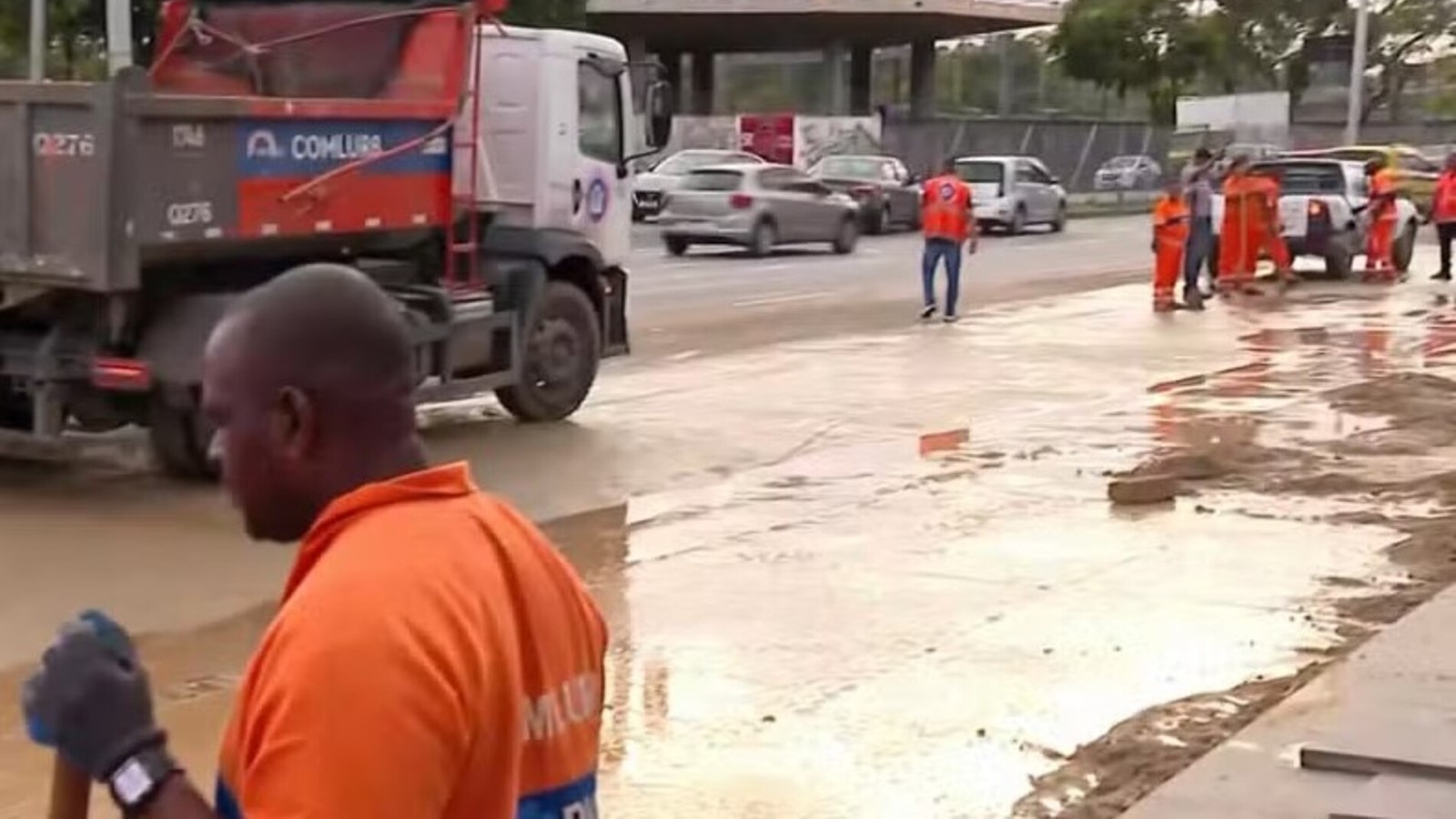 Trabalhadores uniformizados e caminhão Comlurb em rua com água e lama